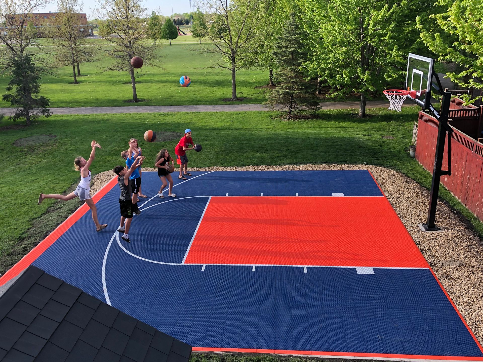 Children playing basketball on an outdoor court. Court is blue and red. Some are shooting hoops.