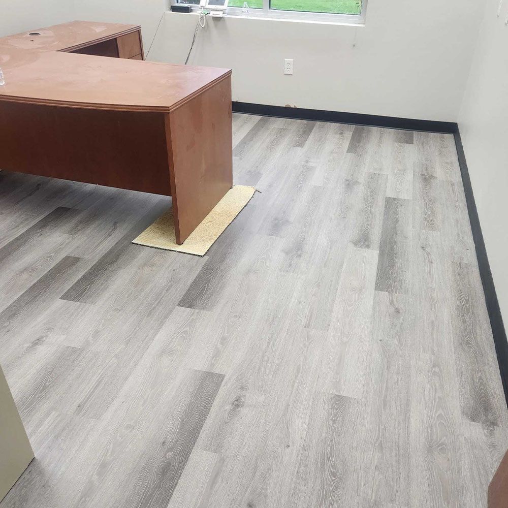 Office interior with wood-look gray flooring, brown desk, and white walls.