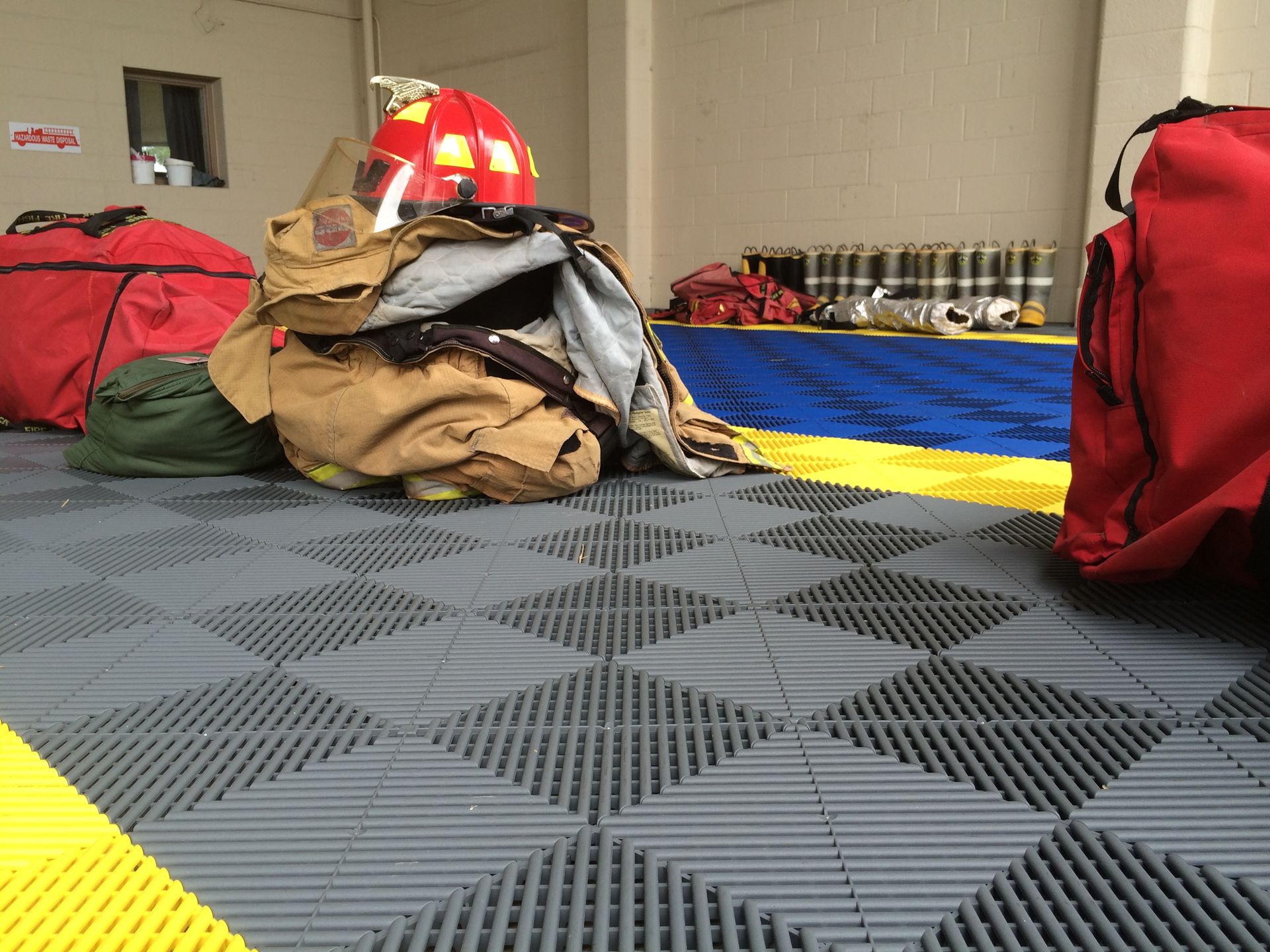 Firefighter gear and bags on a tiled floor in a fire station.