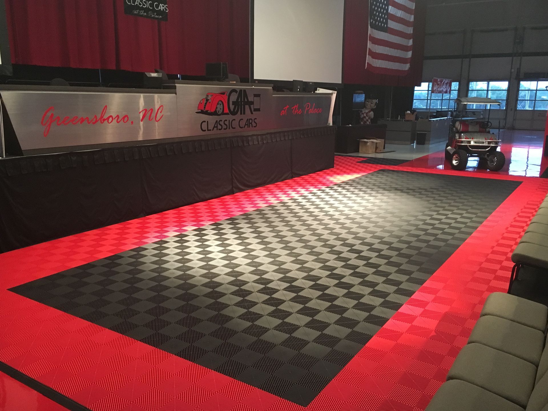 Red and black checkered flooring in a large garage-like space. An American flag hangs above a golf cart.