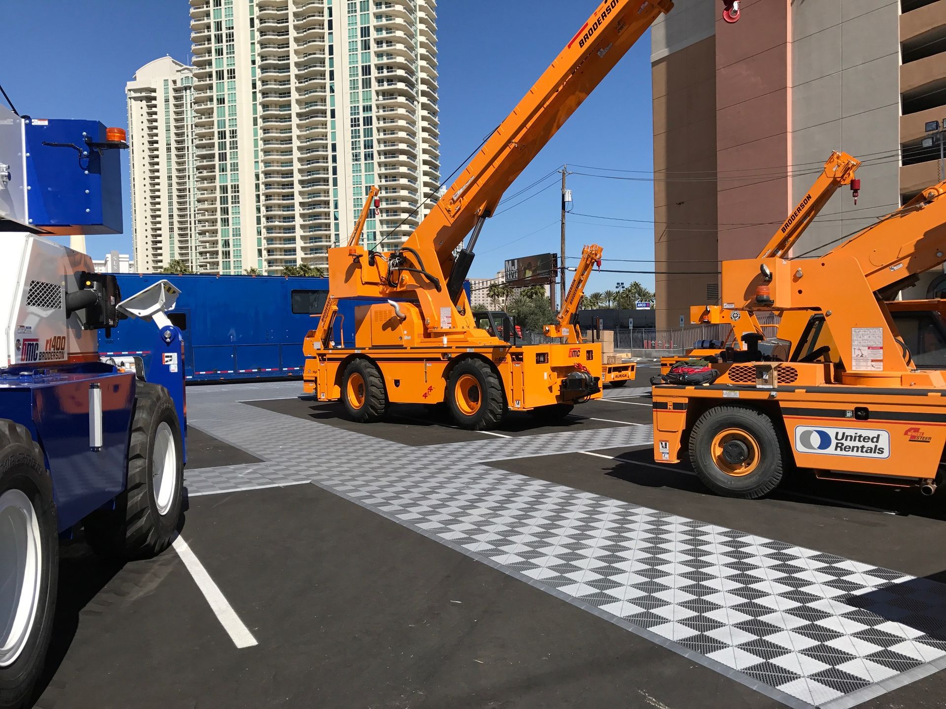 Orange construction cranes on checkered surface in urban setting.