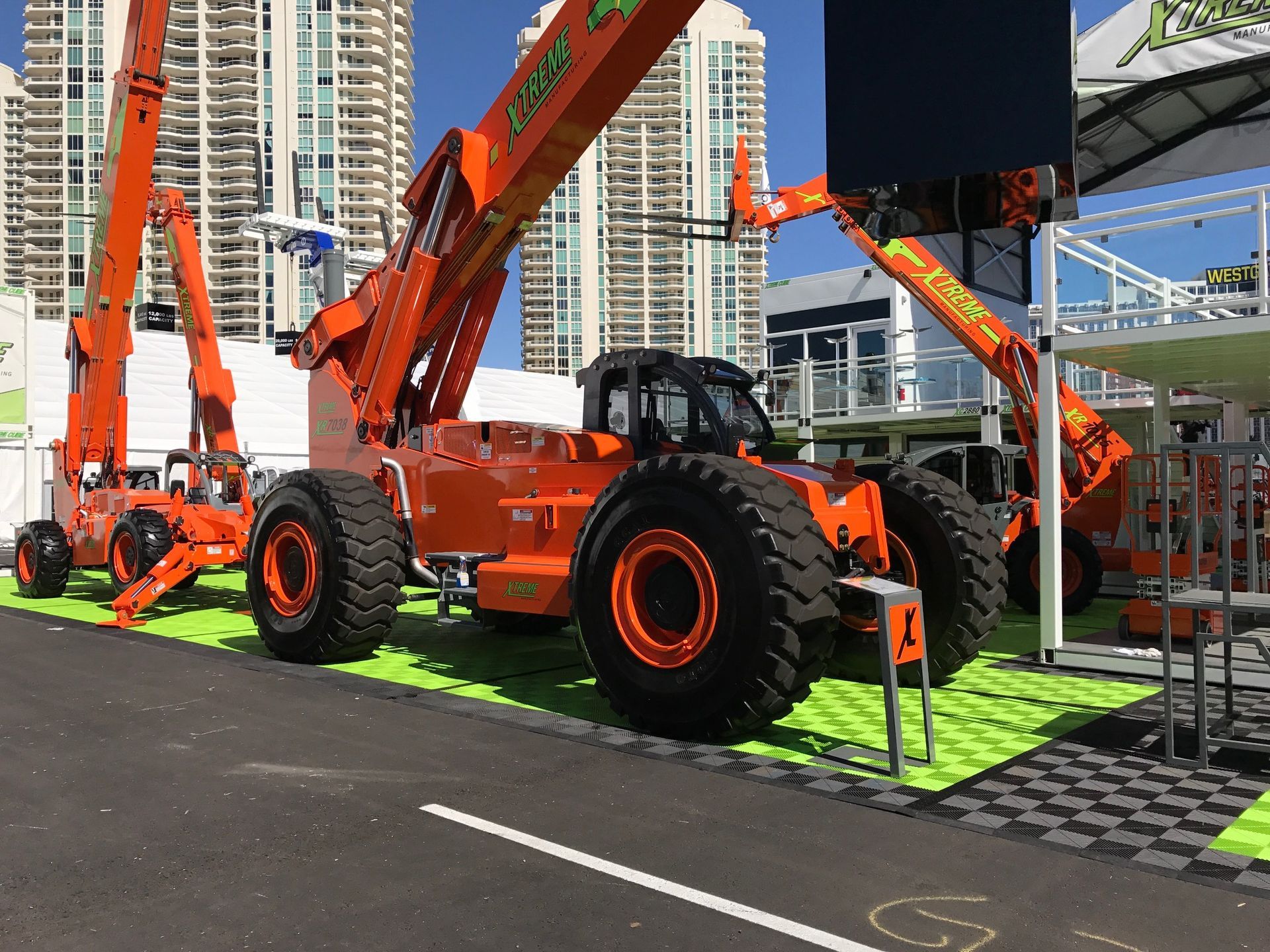 Orange construction vehicles with large tires on display outdoors with high-rise buildings in the background.