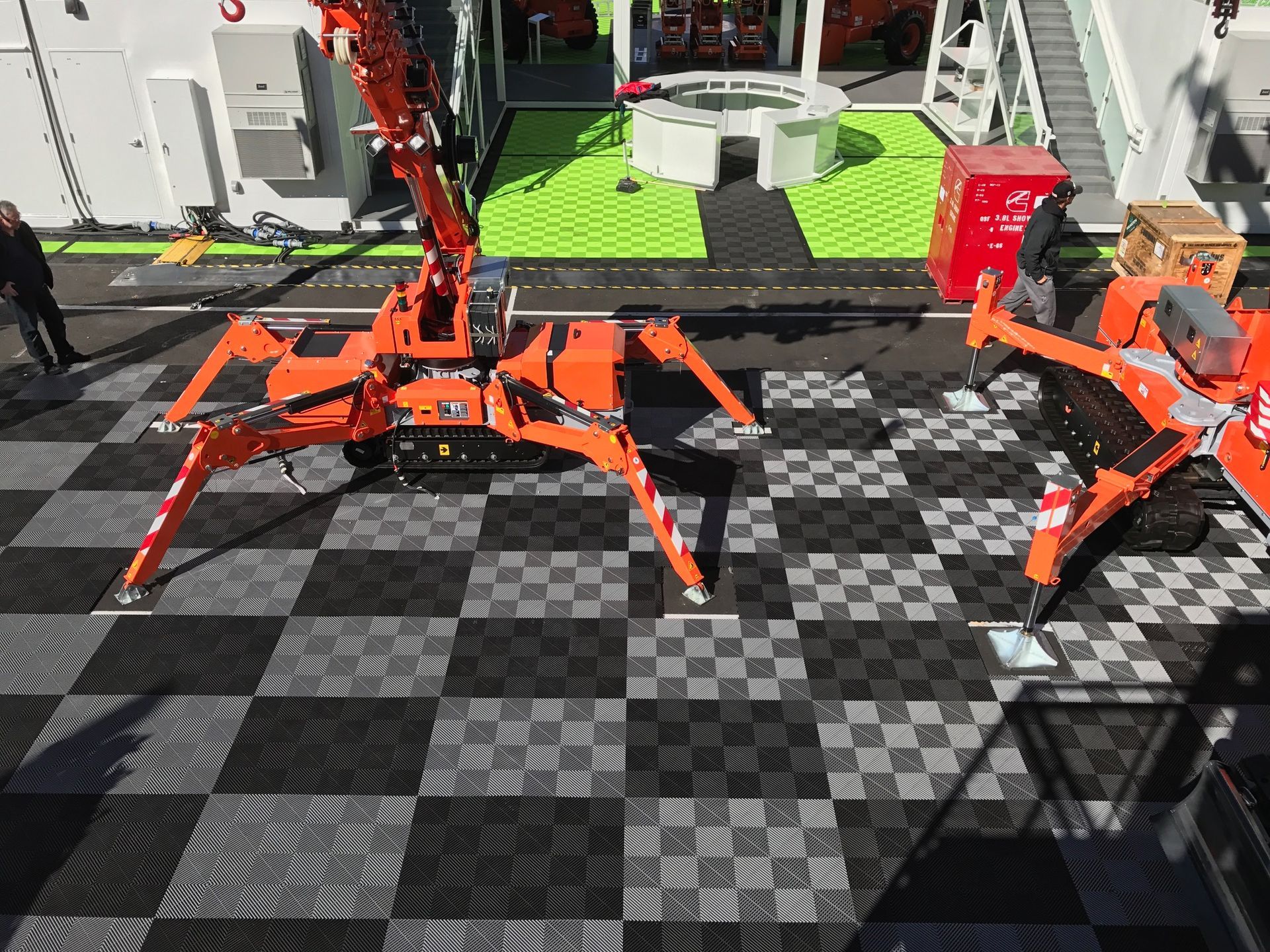 Orange spider-like crane on checkered floor, another crane visible to the right, outdoor setting.