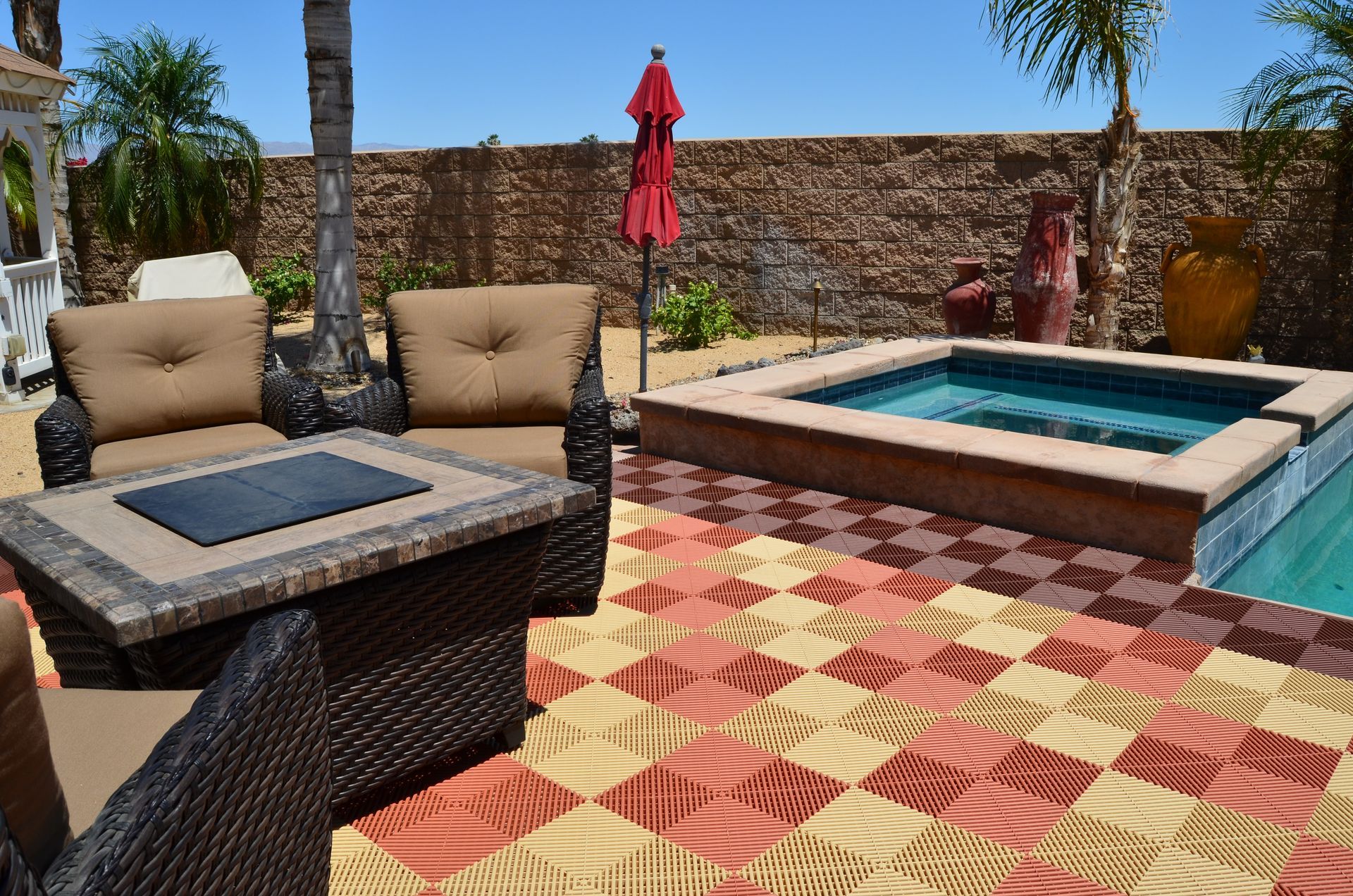Patio with wicker furniture, hot tub, red umbrella, and colorful patterned tiles.