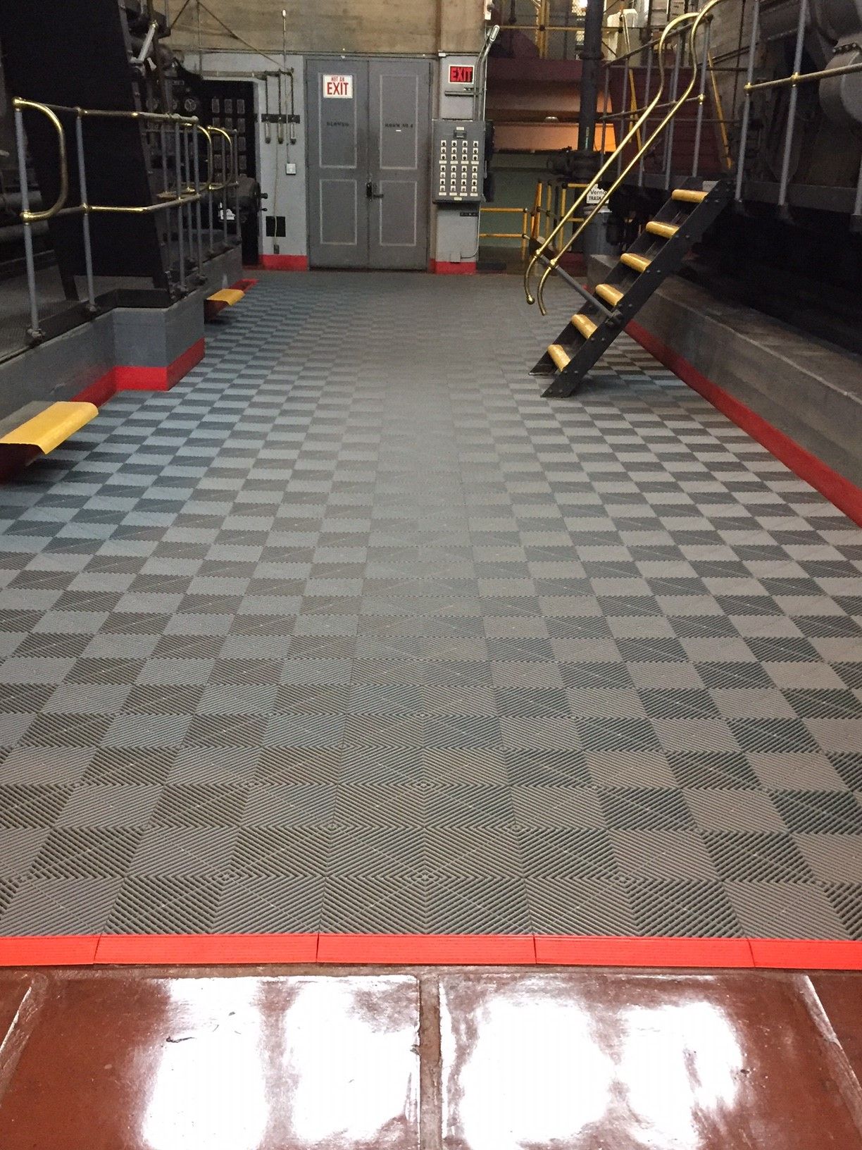 Checkered floor in industrial setting with stairs, machinery, and red trim.