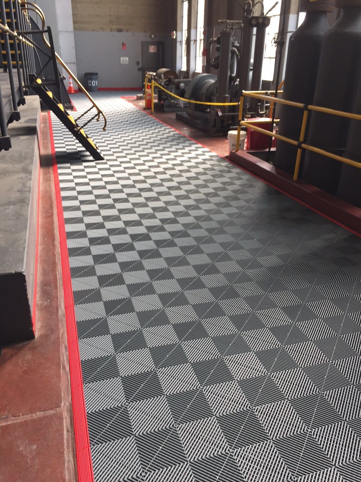 Checkered floor pathway in a machinery room, bordered by red and gray.