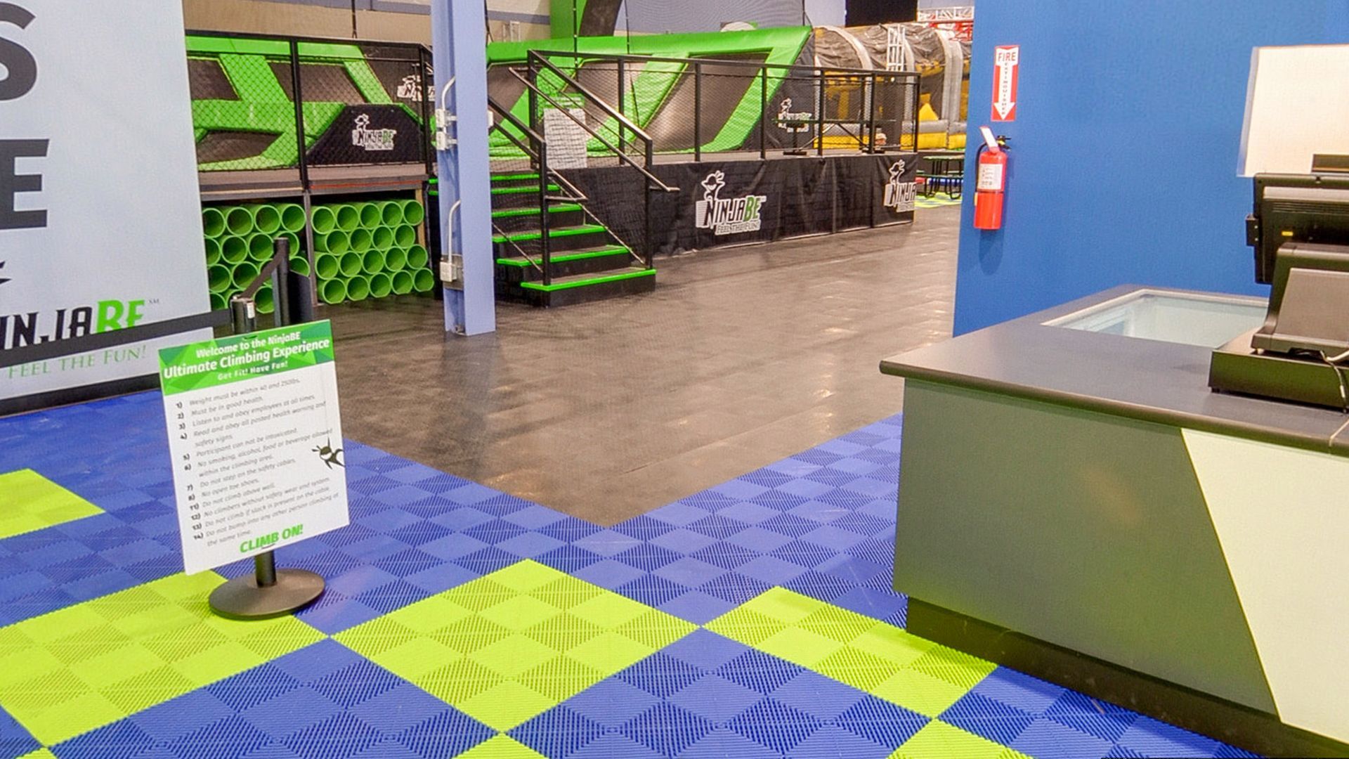 Entrance to a trampoline park with green and blue floor tiles and a sign.