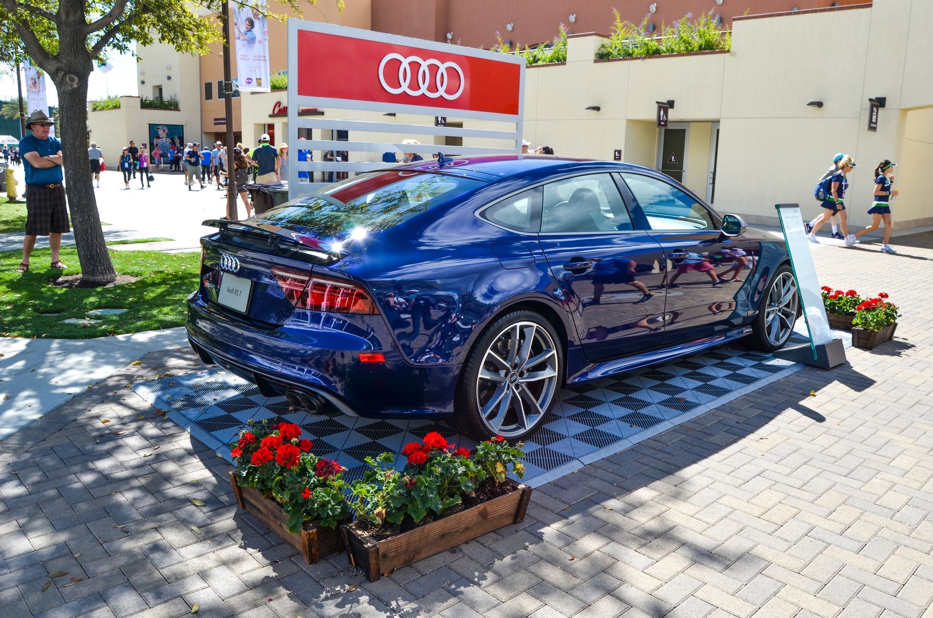 Blue Audi RS7 on display, outdoors with Audi logo and people in background.
