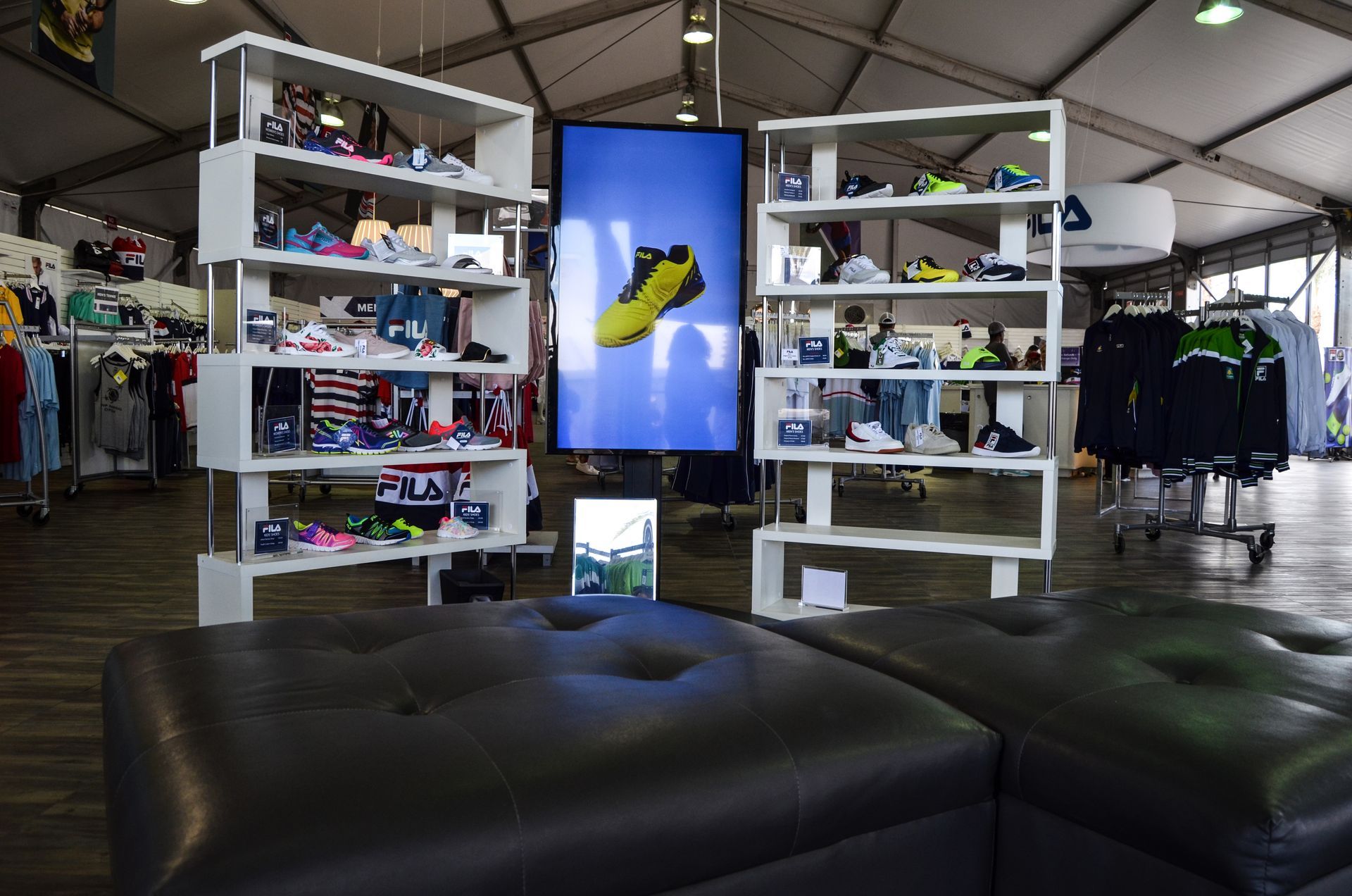Inside a tent, a shoe store display with shelves of shoes and a large screen displaying a shoe.