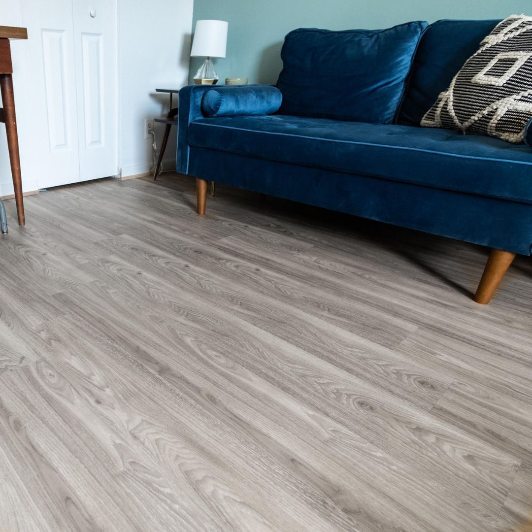 Light gray wood-look flooring in a room with a teal velvet couch, a white door, and a table.