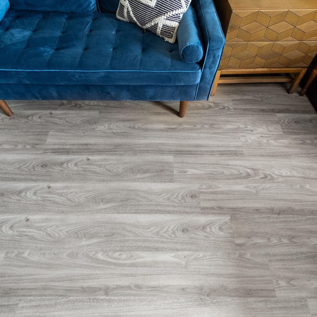Blue velvet sofa and wooden side table on gray wood-look flooring.