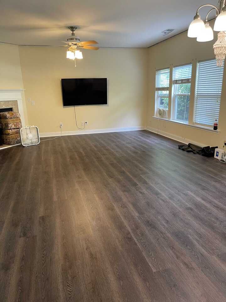 Empty living room with dark wood-look flooring, beige walls, and a mounted TV.