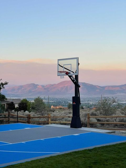 Basketball hoop on a blue and gray court with mountain backdrop at dusk.