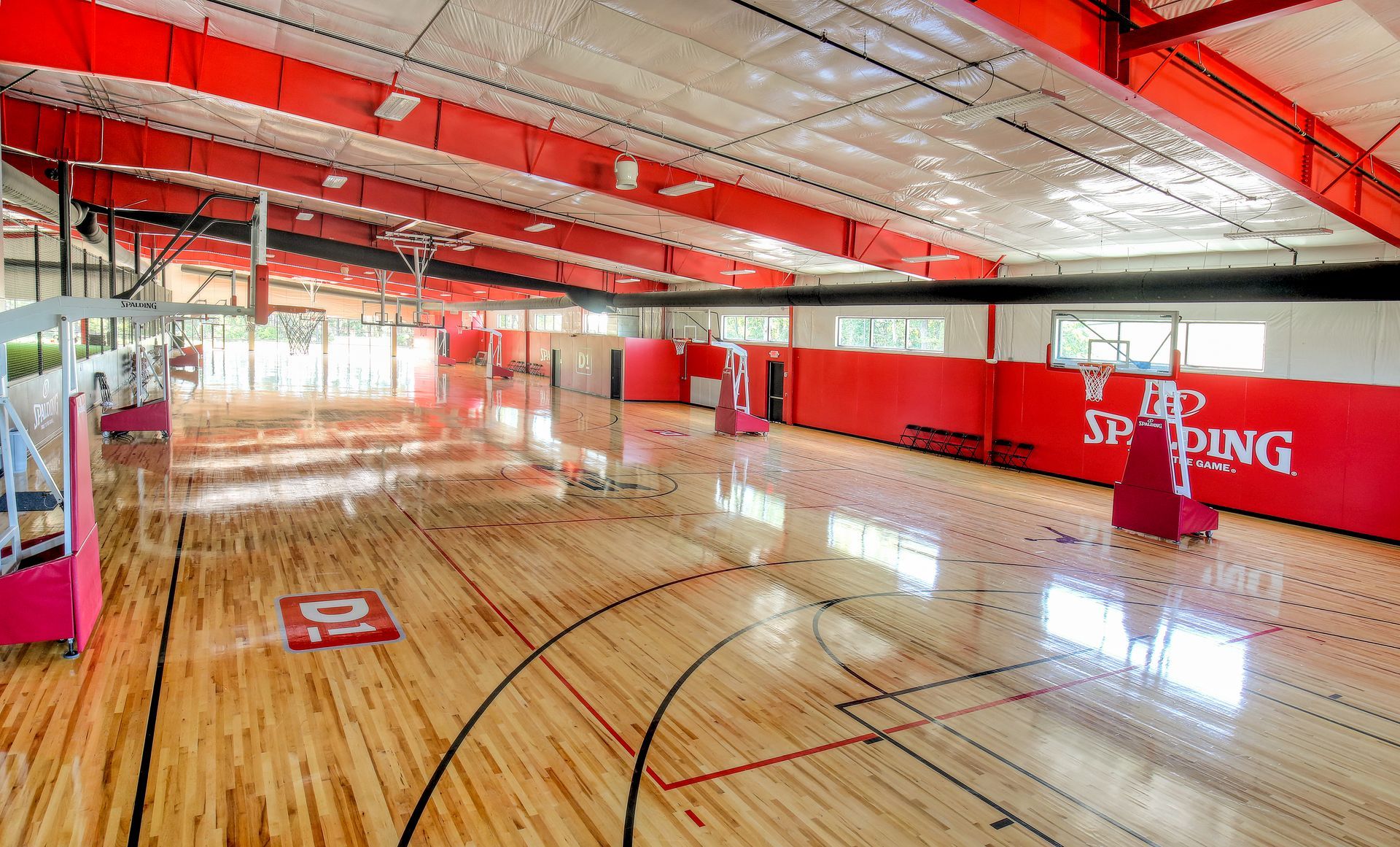 Basketball court with wooden floor, red accents, and natural light.