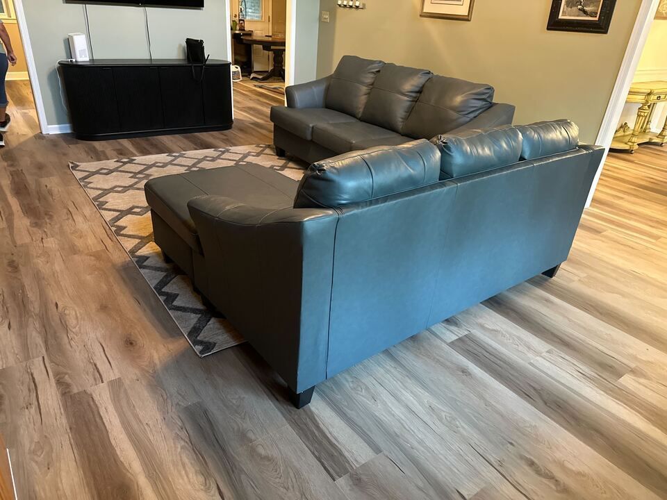 Gray leather sectional sofa on a patterned rug, set in a living room with wood-look flooring.