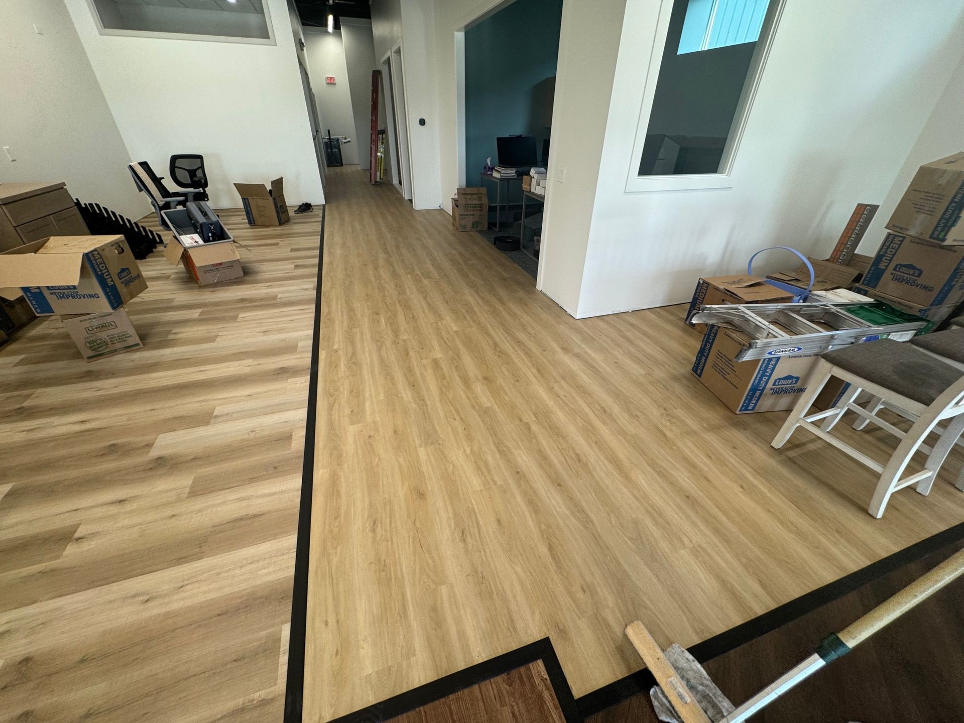 hallway with newly installed wood-looking flooring, boxes, and a broom