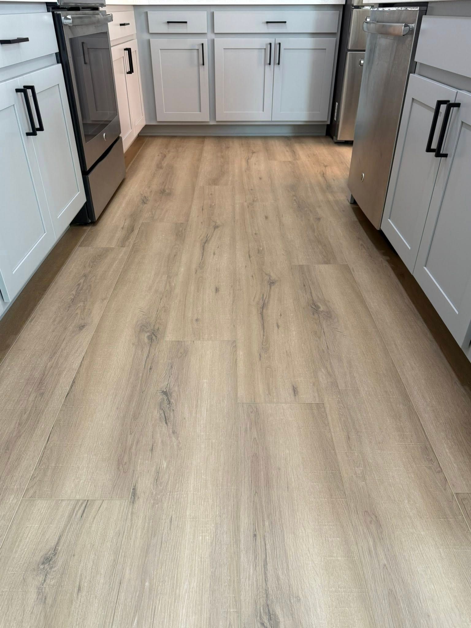kitchen floor with light brown wood-look planks, white cabinets, and stainless steel appliances