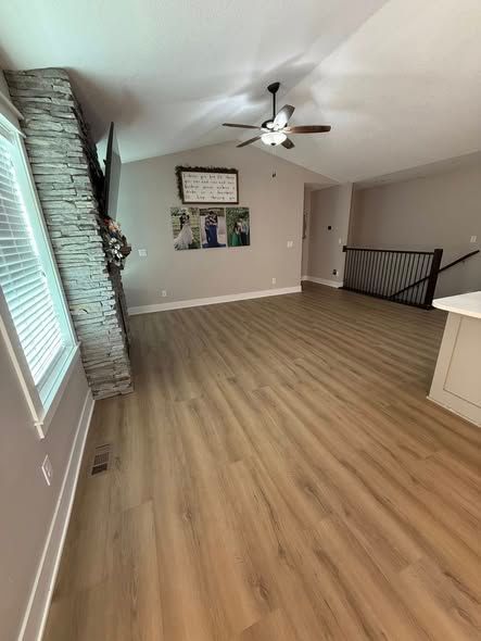 living room with wood floors, stone fireplace, vaulted ceiling, and artwork
