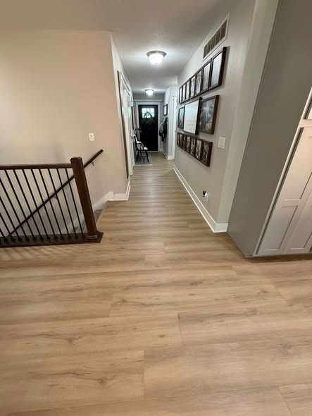 long hallway with light wood-looking flooring, staircase, framed photos on wall, and door at end