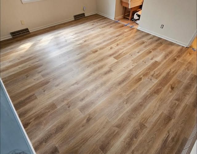 light brown wood-looking flooring installed in a room, with natural light and air vents visible along the wall