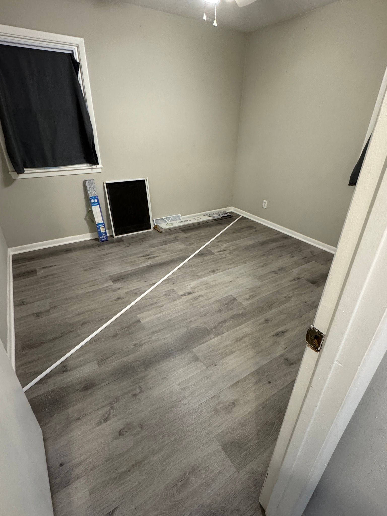 empty room with gray flooring and walls, a window with a curtain, and a door frame