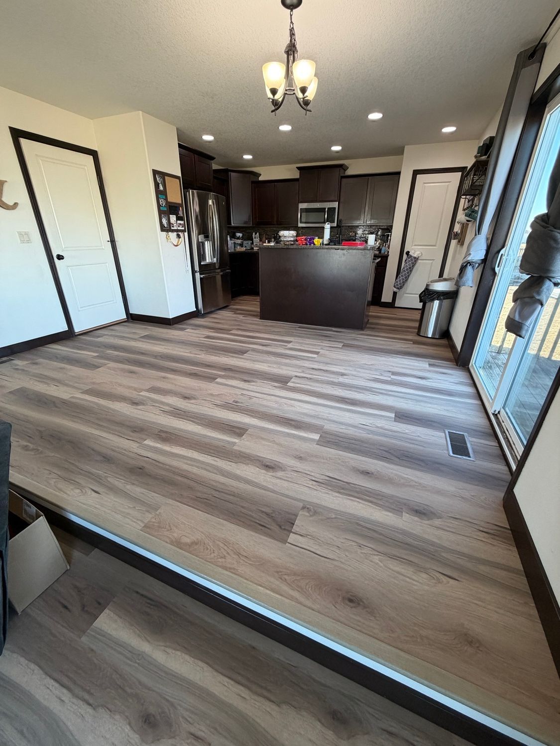 Open kitchen and living area with wood-look floors, dark cabinets, and ceiling lights.