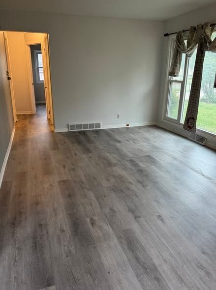 empty room with gray wood-looking flooring, light gray walls, and a window with a curtain