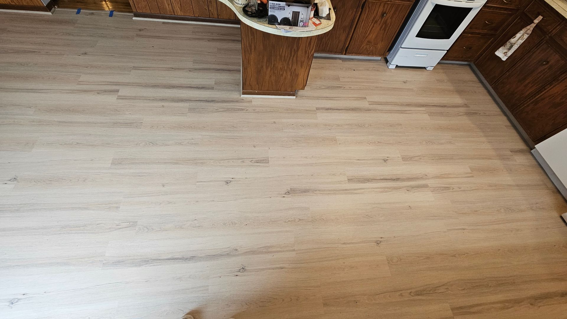 Empty light wood kitchen floor with cabinets along the right wall and a small table near the top center