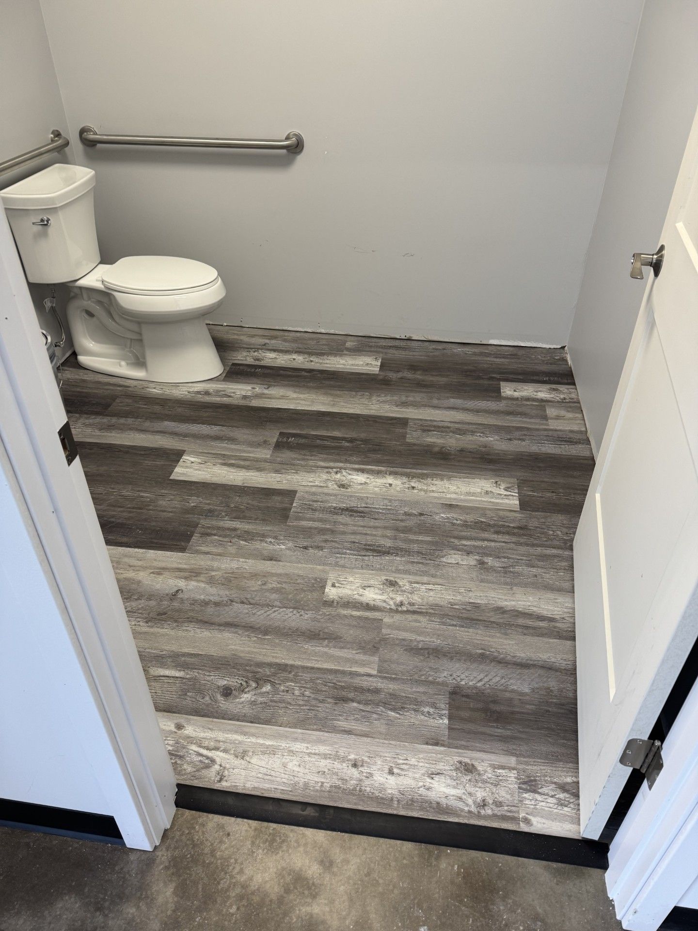 small bathroom with a toilet, grab bar, and wood-looking flooring