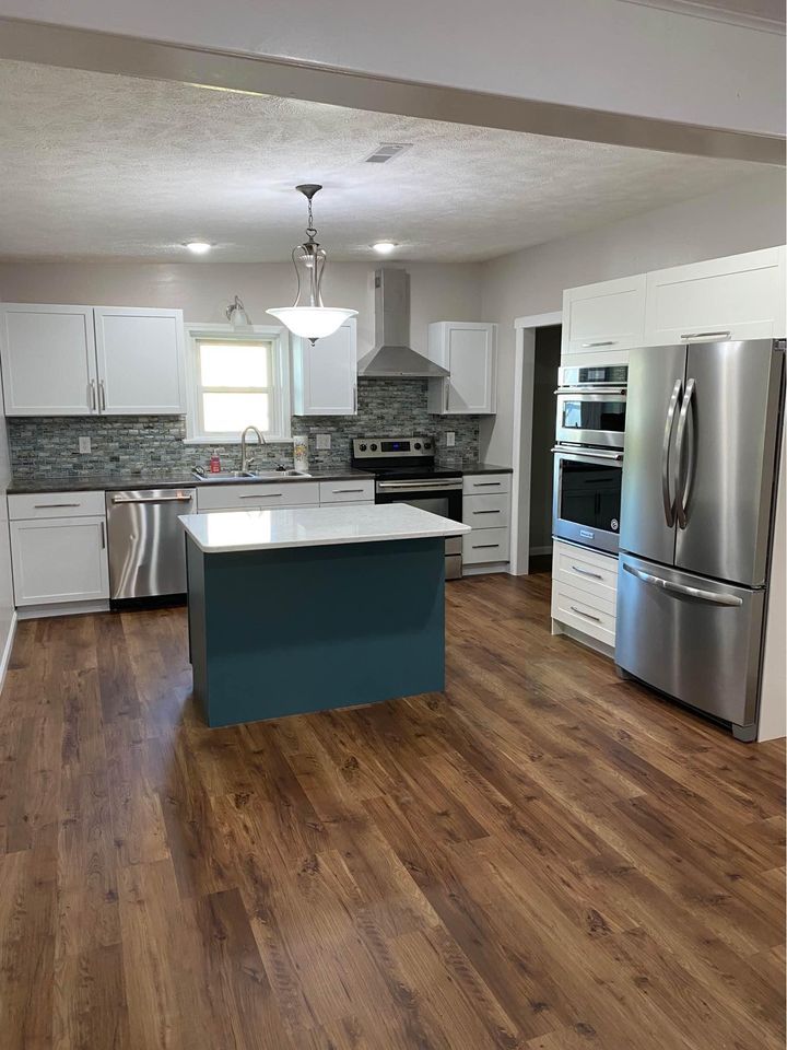 modern kitchen with white cabinets, blue island, stainless steel appliances, and wood-looking flooring