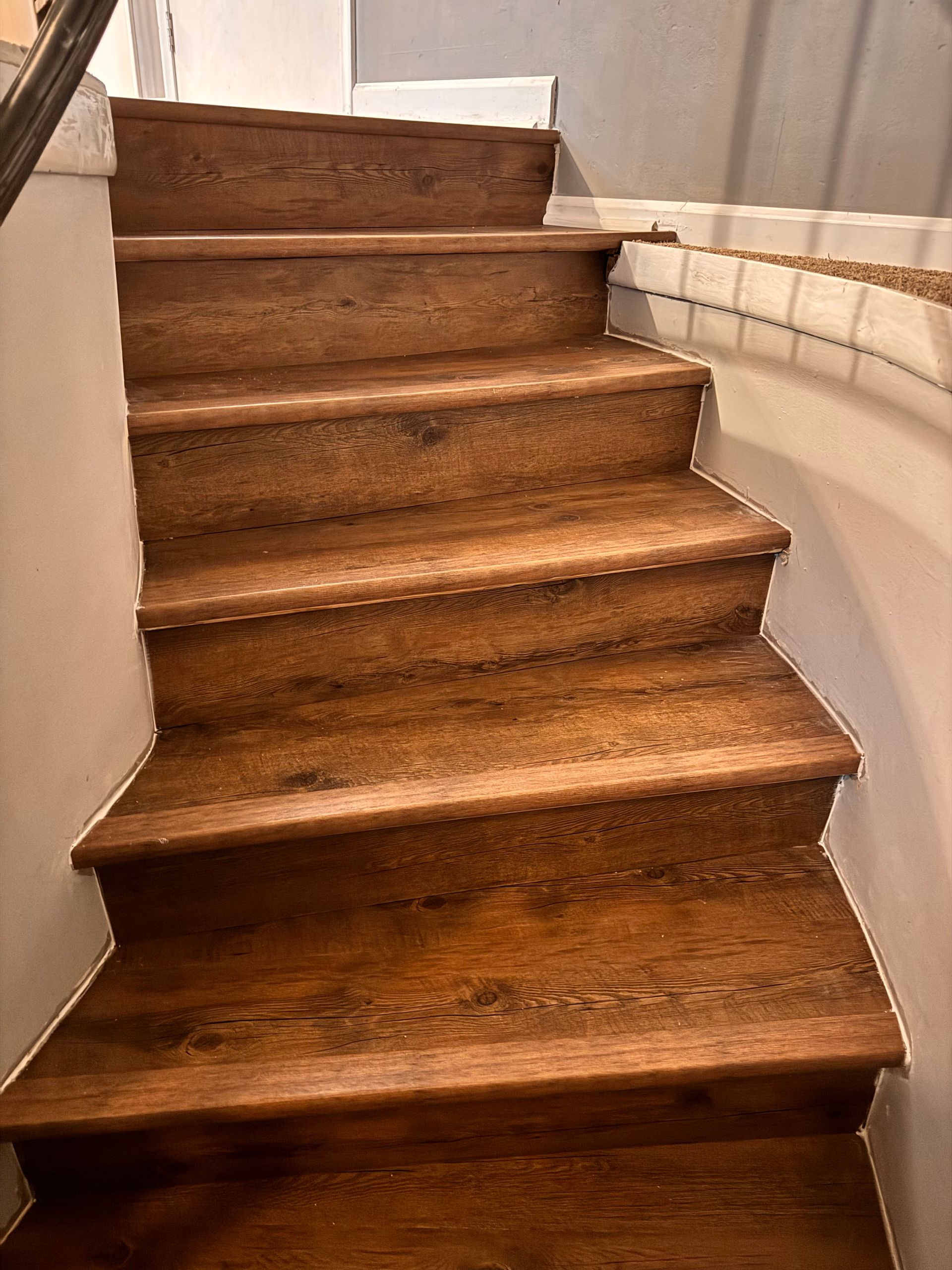 Narrow wooden staircase with carpeted steps and a white handrail in a dim hallway