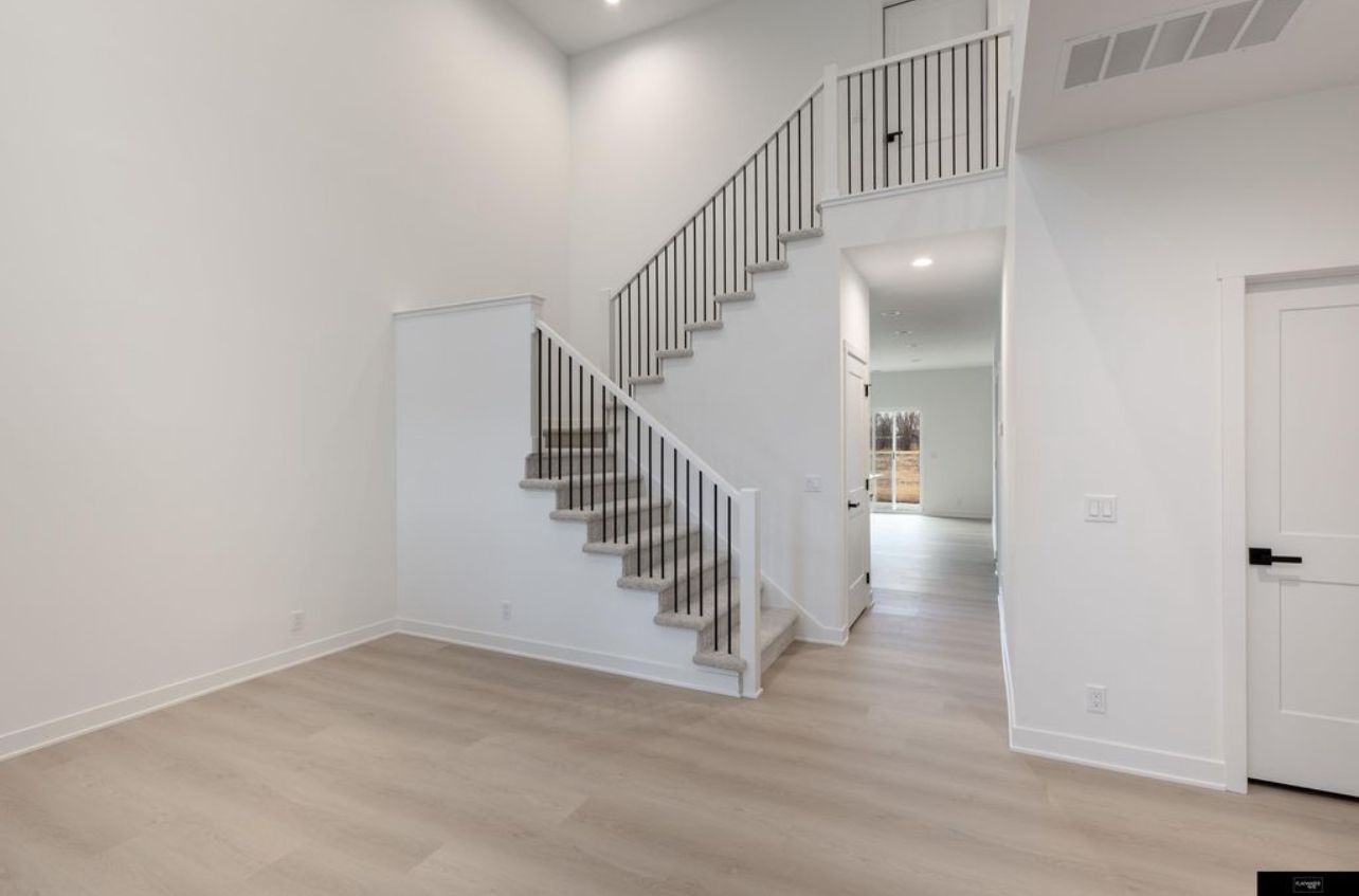 Bright empty foyer with light wood floors, white walls, staircase, and hallway view