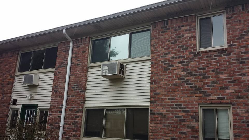 A two-story apartment building exterior featuring red brick, cream-colored siding, and window air conditioning units.
