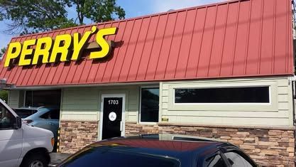 The front of Perry's business, featuring a red metal roof, light green walls, a stone base, and parked cars.