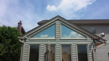 Light grey siding house exterior featuring a large, triangular multi-paned window above standard rectangular windows.