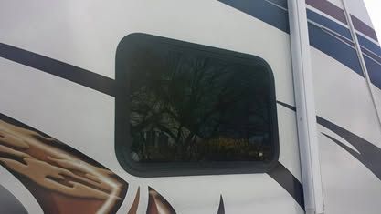 A tinted rectangular window set into the exterior wall of a white RV with decorative dark graphic decals.