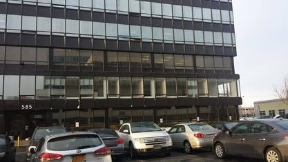 A multi-story dark building at 585, with a parking lot in front containing several cars.