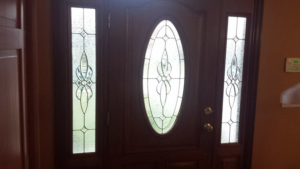 A wooden front door with an oval glass panel and matching sidelights featuring decorative leaded glass designs.