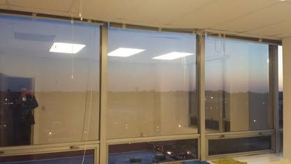 Large office windows with reflections of overhead lights and a sunset sky, looking out over a distant horizon.
