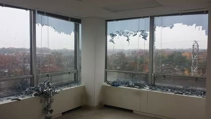 Corner office with shattered upper window panes and broken glass scattered along the interior window ledge.