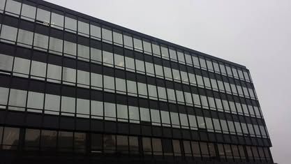 Low-angle view of a modern building facade with repetitive rows of rectangular windows against an overcast sky.