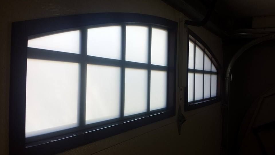 A garage door with arched, frosted windows looking out onto a bright light.
