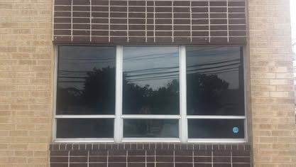 A rectangular window with a dark glass tint, divided into six panels by a white frame, set in a tan and brown brick wall.