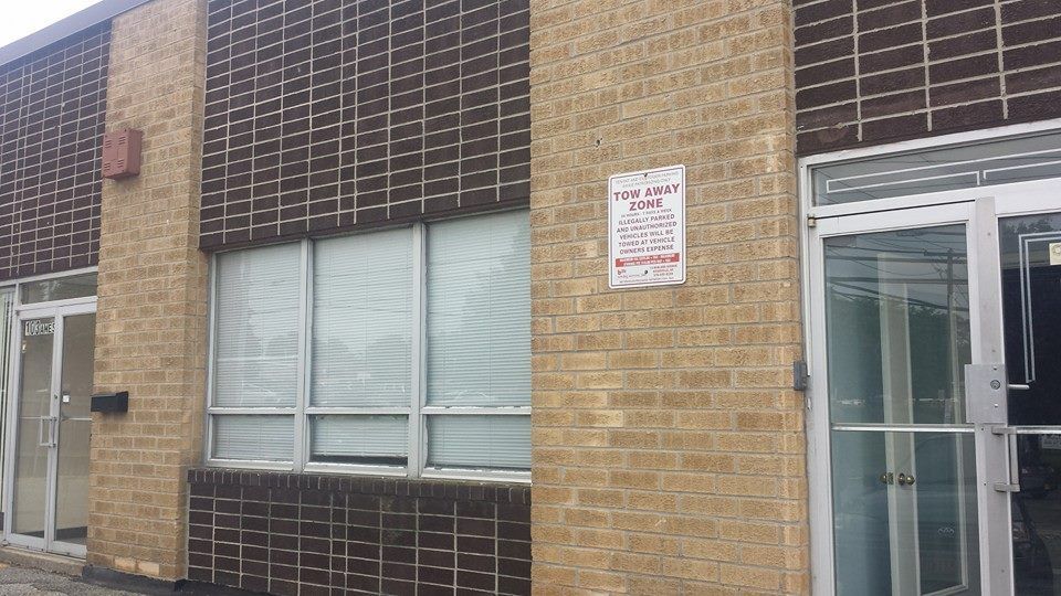 A brick building exterior featuring glass doors and windows, with a small white sign posted on the wall.