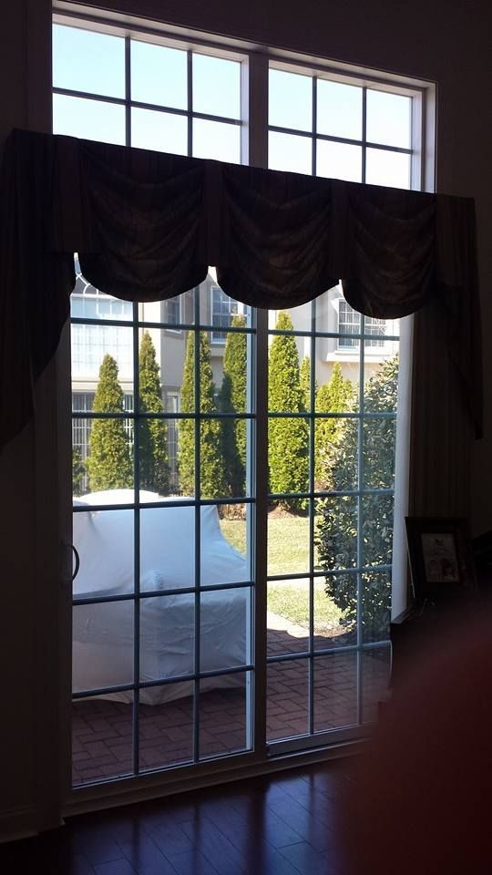A large sliding glass door with a decorative brown scalloped valance looks out onto a patio with covered outdoor furniture.