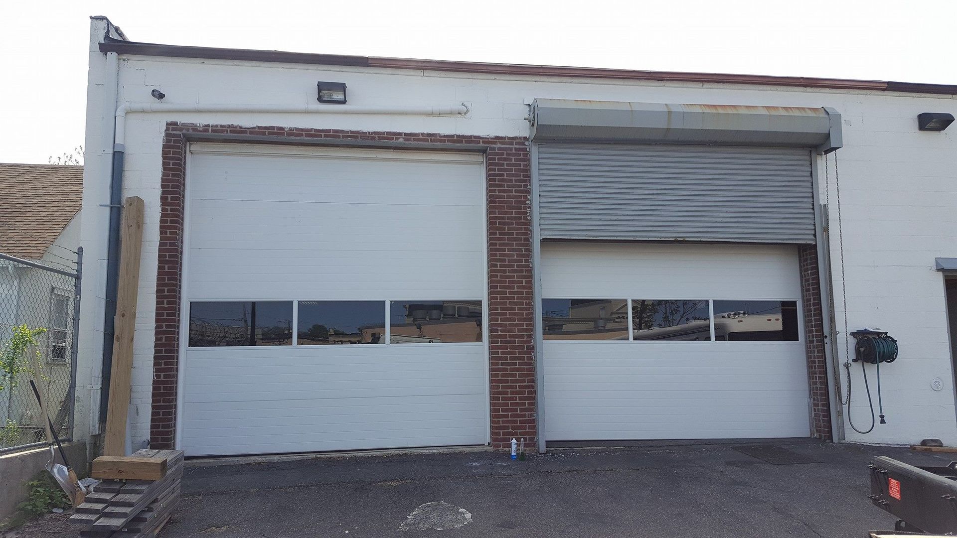 Two side-by-side garage doors with windows on a white building exterior, with one door partially open.