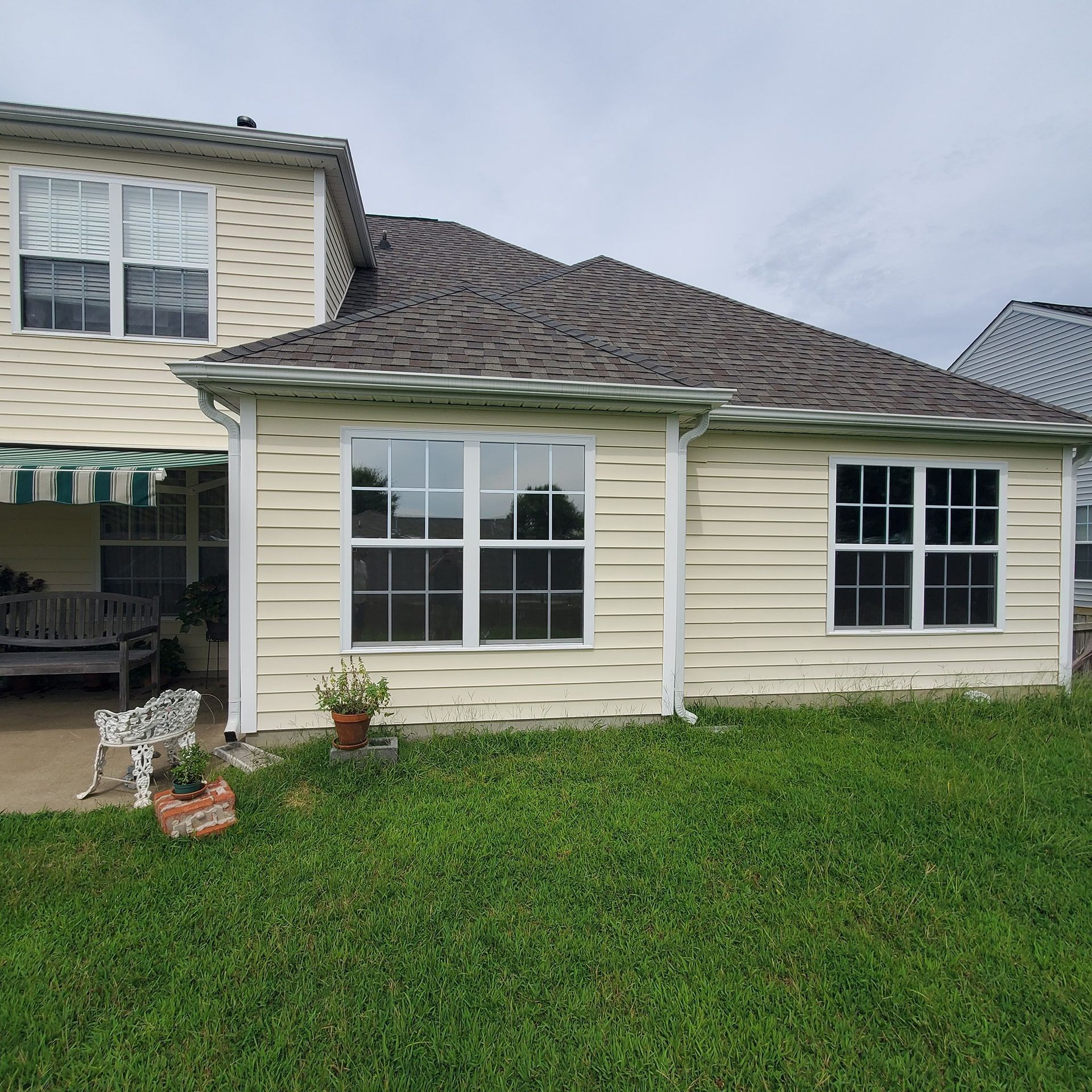 A two-story house with cream-colored siding and a dark grey shingled roof, featuring several multi-pane windows.