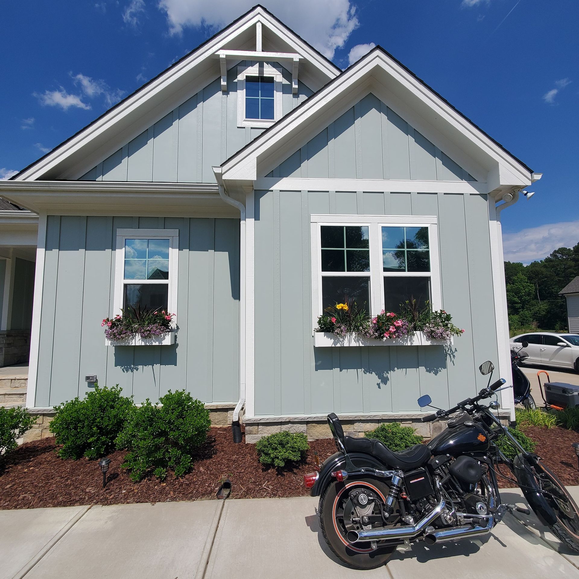 A light blue cottage-style house with board-and-batten siding, flower boxes, and a black motorcycle parked in the front.