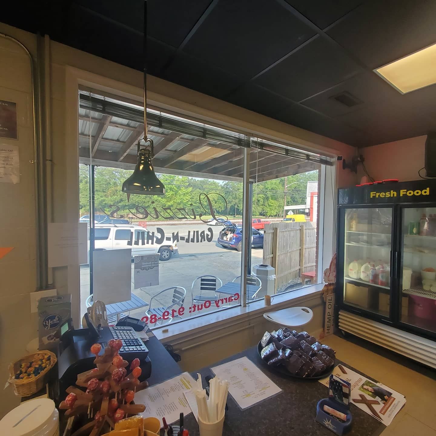 A view from behind the counter of a small diner looking out onto a parking lot and trees through a large window.
