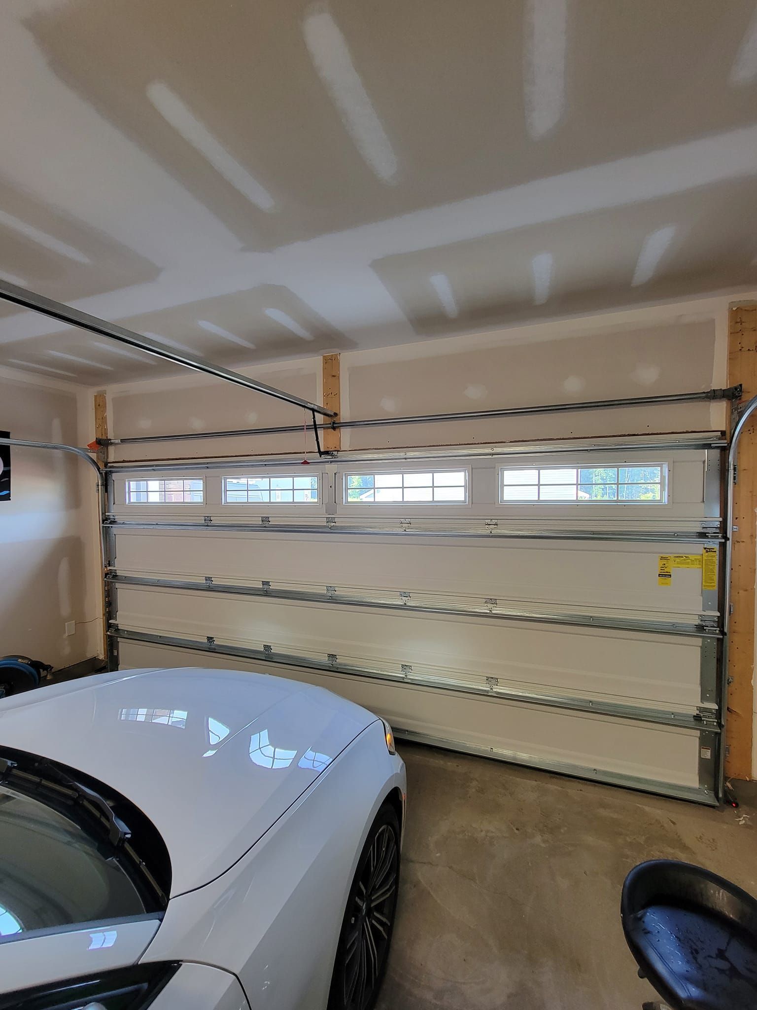 An interior view of a garage showing a closed white sectional garage door with a row of small windows near the top.